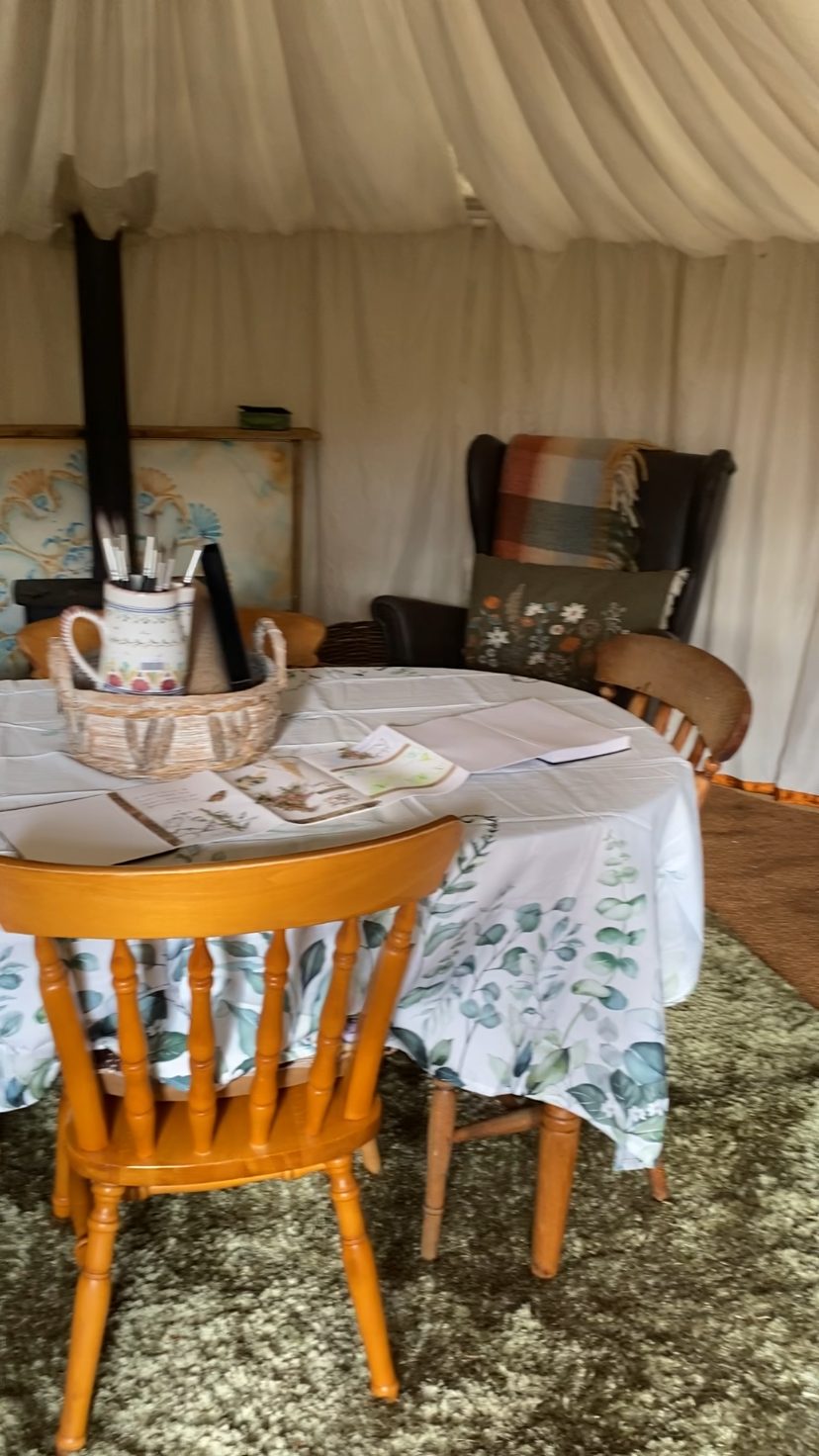 A concertina artist's book opened on the yurt table beside a basket of paintbrushes