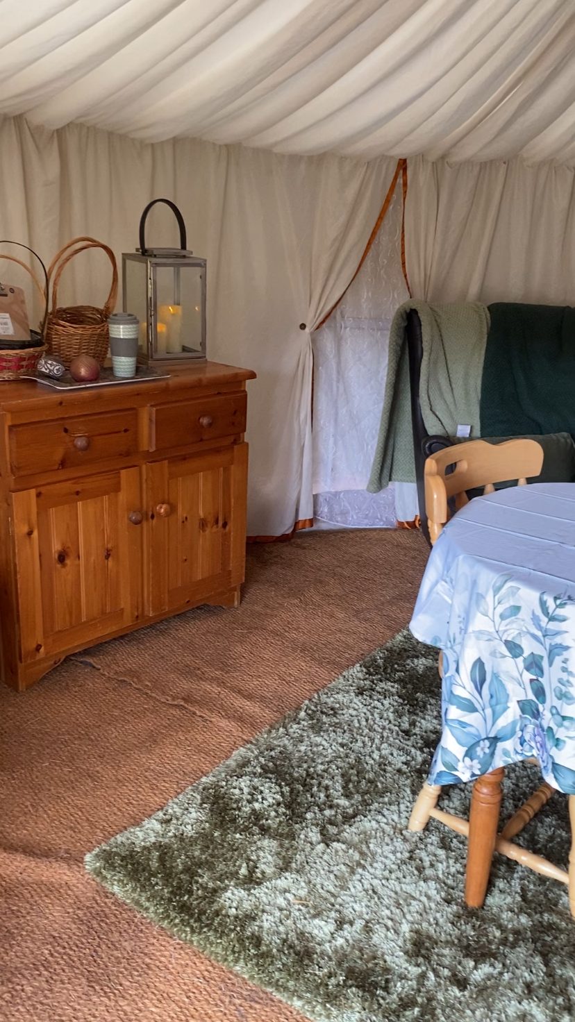 A cosy corner of the yurt with a pine sideboard, armchair and soft green throws